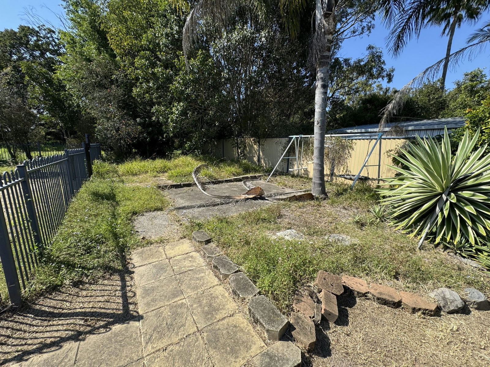 Paved courtyard at a Marsden property with weeds growing through the pavers and rock edging