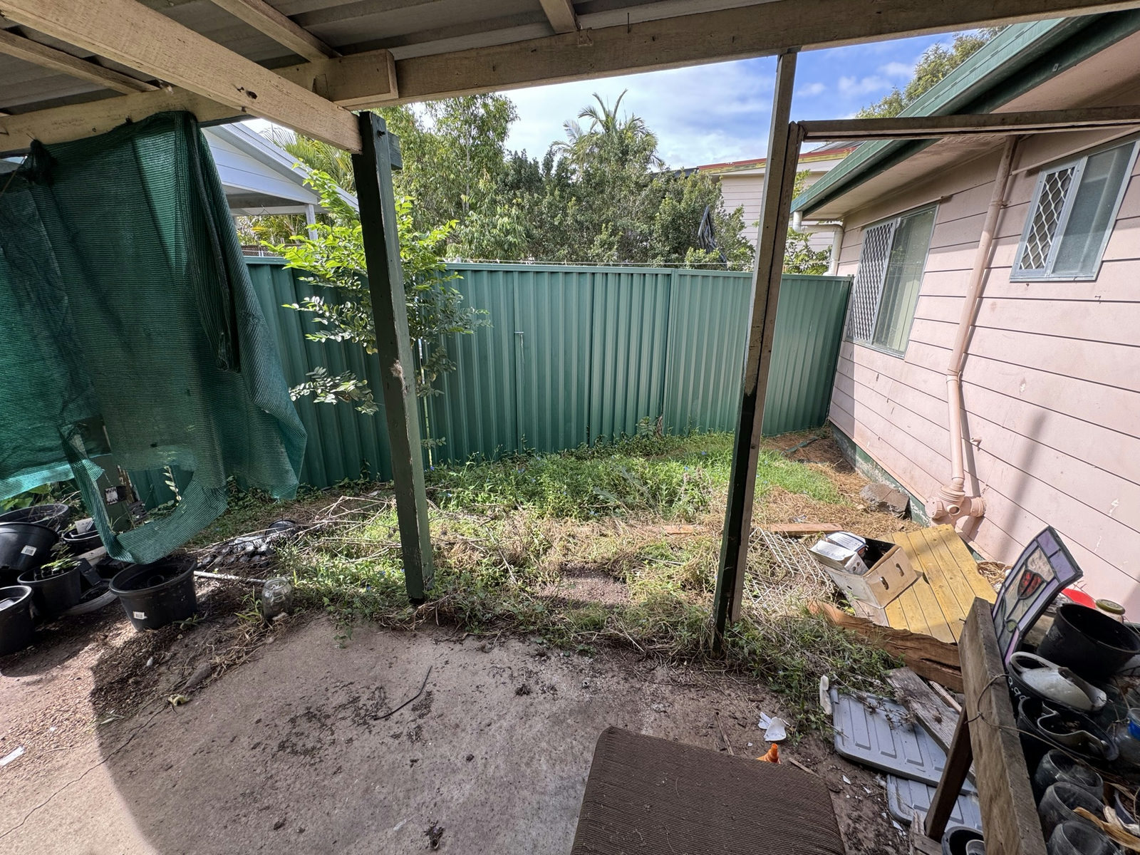 Debris and overgrowth built up under a carport at a neglected Waterford West property